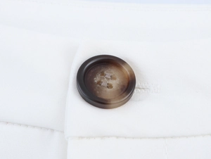 Detail of a brown amber button and fine stitching on white twill fabric trousers