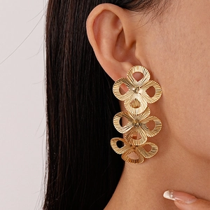 Close-up of golden triple floral drop earrings with textured petal details and fringe