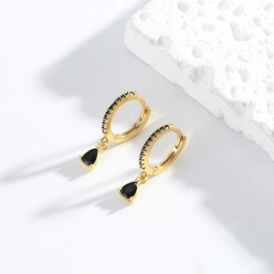 Macro shot of gold teardrop earrings with black stones and fine brushed metal texture