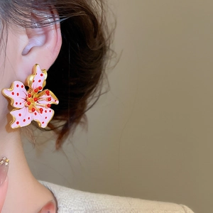 Detailed close-up of pink flower earrings with red dots and gold-toned edges on model