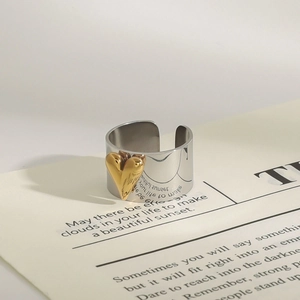 Detailed view of silver open ring with 3D gold heart accent on aesthetic paper