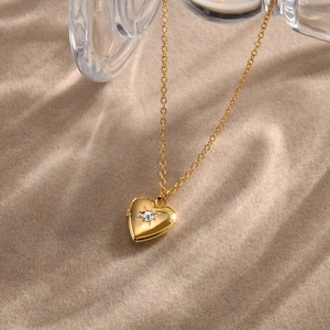 Artistic close-up of a gold heart locket necklace with zircon on a beach setting