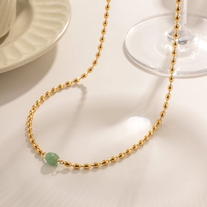 Detail of a 18K gold stainless steel beaded necklace with a green oval stone pendant