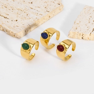Gold wide-band rings with oval natural stones in green, blue, and red on travertine
