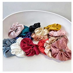Dettaglio macro di elastici per capelli in raso setoso in vari colori tra cui bordeaux e rosa