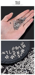 Vista macro di 26 ciondoli a forma di lettera in acciaio inox argento per gioielli fai da te