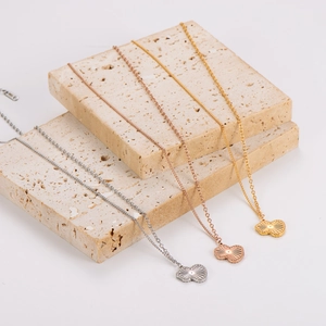 Three heart-shaped scallop necklaces in silver, rose gold, and gold on beige stone