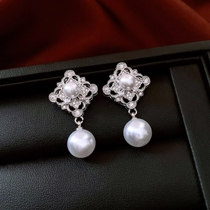 Detail of silver rhombic hollow earrings with crystals and hanging pearl on dark background