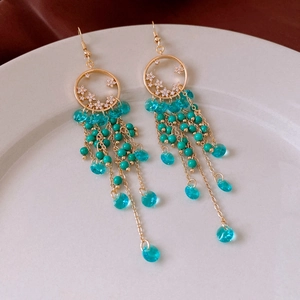 Detail of bohemian gold earrings with turquoise beads and crystal tassels on white tray
