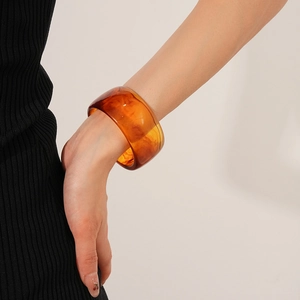 Close-up of a wide amber resin bangle with marble texture worn on the wrist