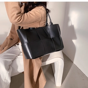 Detailed view of black woven texture leather tote bag carried by a model on a chair
