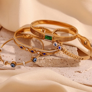 Detail of 18K gold-plated bracelets featuring evil eye motifs and green gemstones