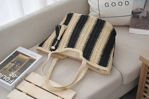 Detailed view of woven straw tote bag featuring black stripes and a fringe tassel