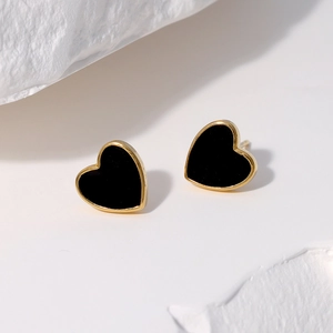 Minimalist gold-plated heart stud earrings with black enamel inlay on white stone pedestal