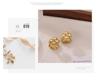 Detail of gold four-leaf clover earrings displayed on soft white fabric with dried flowers