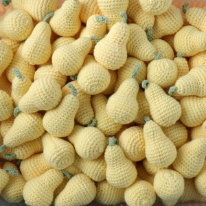 Close-up of bulk handmade crochet yellow pears with green stems in knitted wool