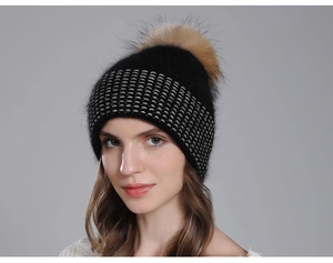 Detail view of black knit beanie with silver accents and large raccoon fur pom-pom