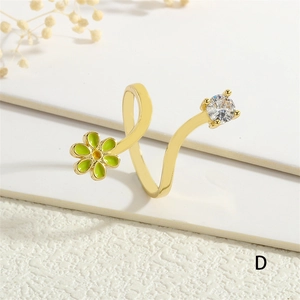 Detail of gold wavy ring featuring a green enamel flower and a sparkling zircon stone