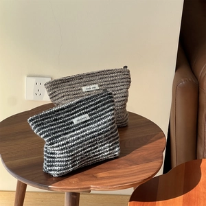 Set of two thick woven makeup bags with stripes and zipper on a wooden table