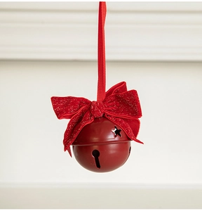 Close-up of matte red metal Christmas bell with star cutouts and a glittery red bow ornament