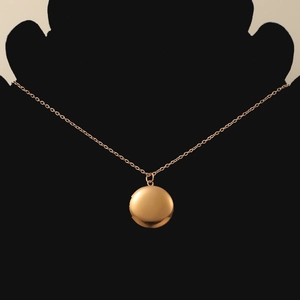 Detail of rose gold round locket pendant on cable chain shown on black neck display