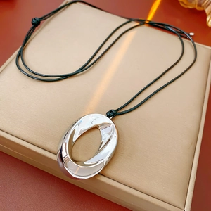Close-up of a silver oval pendant with a black woven cord on a beige jewelry box