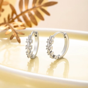 Silver huggie hoop earrings with leaf-shaped zircon accents on a soft background