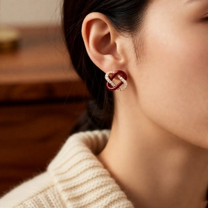 Close-up of elegant gold-plated interlocking earrings with wine red enamel and cubic zirconia