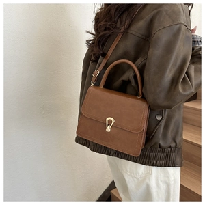 Brown vintage PU leather crossbody bag with gold buckle on a model in a minimal setting