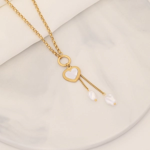 Golden heart pendant necklace with pearl tassels on a minimalist marble background