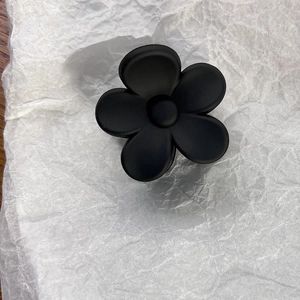 Close-up of matte black five-petal flower hair claw clip on white textured paper