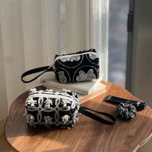 Detail of black embroidered canvas pouch featuring white floral pattern and fringe