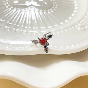 L-shaped bat heart nose stud with red zircon and silver devil wings on ceramic plate