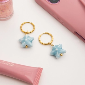 Detail view of 18K gold earrings with blue star pendants featuring marble texture detail
