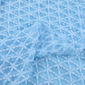 Dettaglio macro del tessuto in pizzo azzurro con motivi floreali e trame multistrato