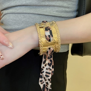 Detail of a wide gold cuff bracelet featuring a leopard print silk scarf intertwined