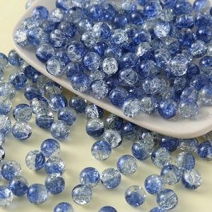 Macro shot of 10mm blue cracked glass beads spilling from a white ceramic plate