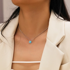 Détail d'un collier en chaîne argentée avec pendentif turquoise carré porté par un mannequin