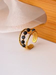 Macro detail of gold-plated open ring with double-layered band and black natural stone beads