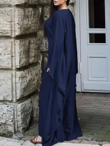 Robe longue bleu foncé élégante à manches longues devant un mur en pierre rustique de qualité