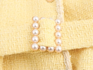 Detailed macro view of a gold buckle with pearls on yellow tweed dress fabric