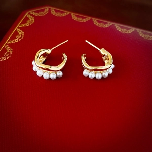 Detailed close-up of golden C-shaped double pearl earrings on a luxury jewelry box