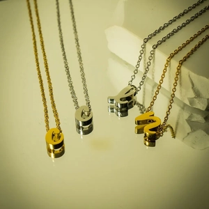 Nahaufnahme minimalistischer Gold- und Silber-Buchstabenanhänger an zarten Ketten