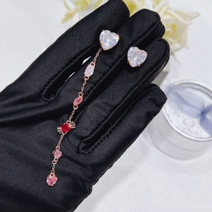 Detailed view of rose gold asymmetrical earrings with pink and red heart-shaped crystals