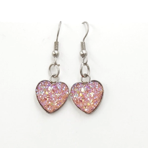 Macro detail of heart-shaped pink glitter earrings with polished silver metal frames
