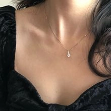 Close-up of minimalist gold necklace with a round sparkling zircon pendant worn on neck