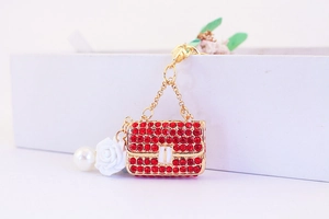 Macro detail of red rhinestone handbag keychain with gold chain and white flower charm