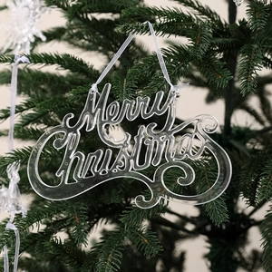 Detail of transparent acrylic Merry Christmas ornament hanging on a lush green Christmas tree