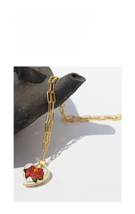 Macro detail of vintage gold heart necklace with white enamel rose and leafy accents