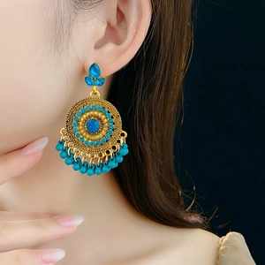 Dettaglio di orecchini vintage dorati con strass blu e nappine indossati da una modella
